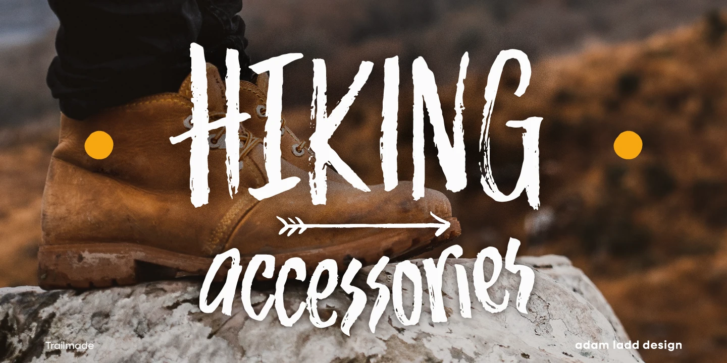 Trailmade font by Adam Ladd Design — the words “HIKING” and “accessories” in a rugged, upright brush script, with an arrow graphic between them, over a hiking boot on a rock