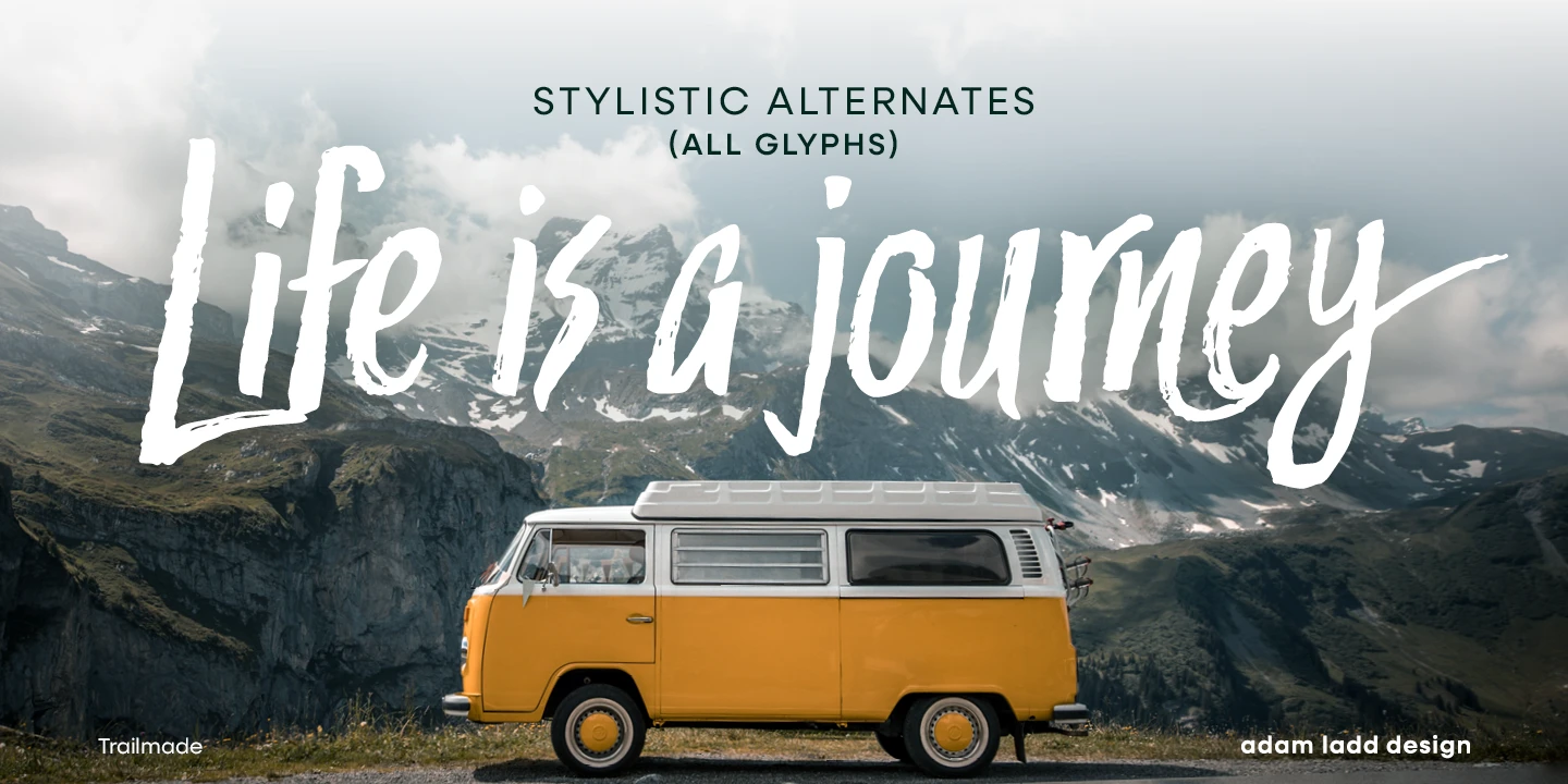Trailmade font by Adam Ladd Design — the words “Life is a journey” in a connected brush script over a yellow camper van and a mountain landscape, with “STYLISTIC ALTERNATES (ALL GLYPHS)” in sans-serif capitals above